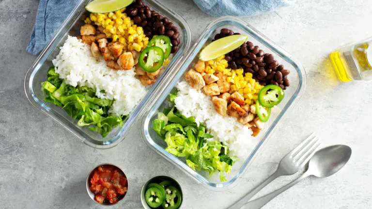 Two glass bowls filled with a complete meal of rice, veggies, meat, and beans